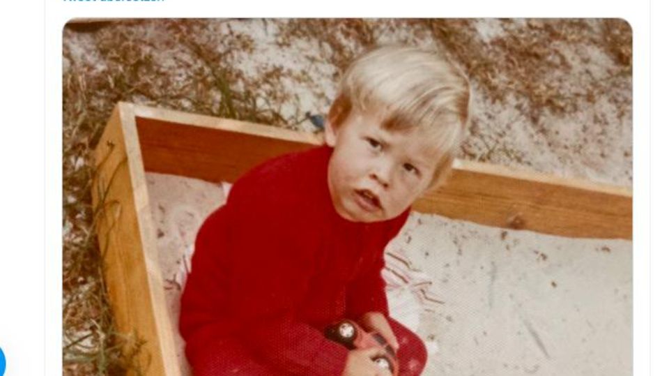 Elon Musk sitzt als dreijähriger blonder Junge in einem Sandkasten