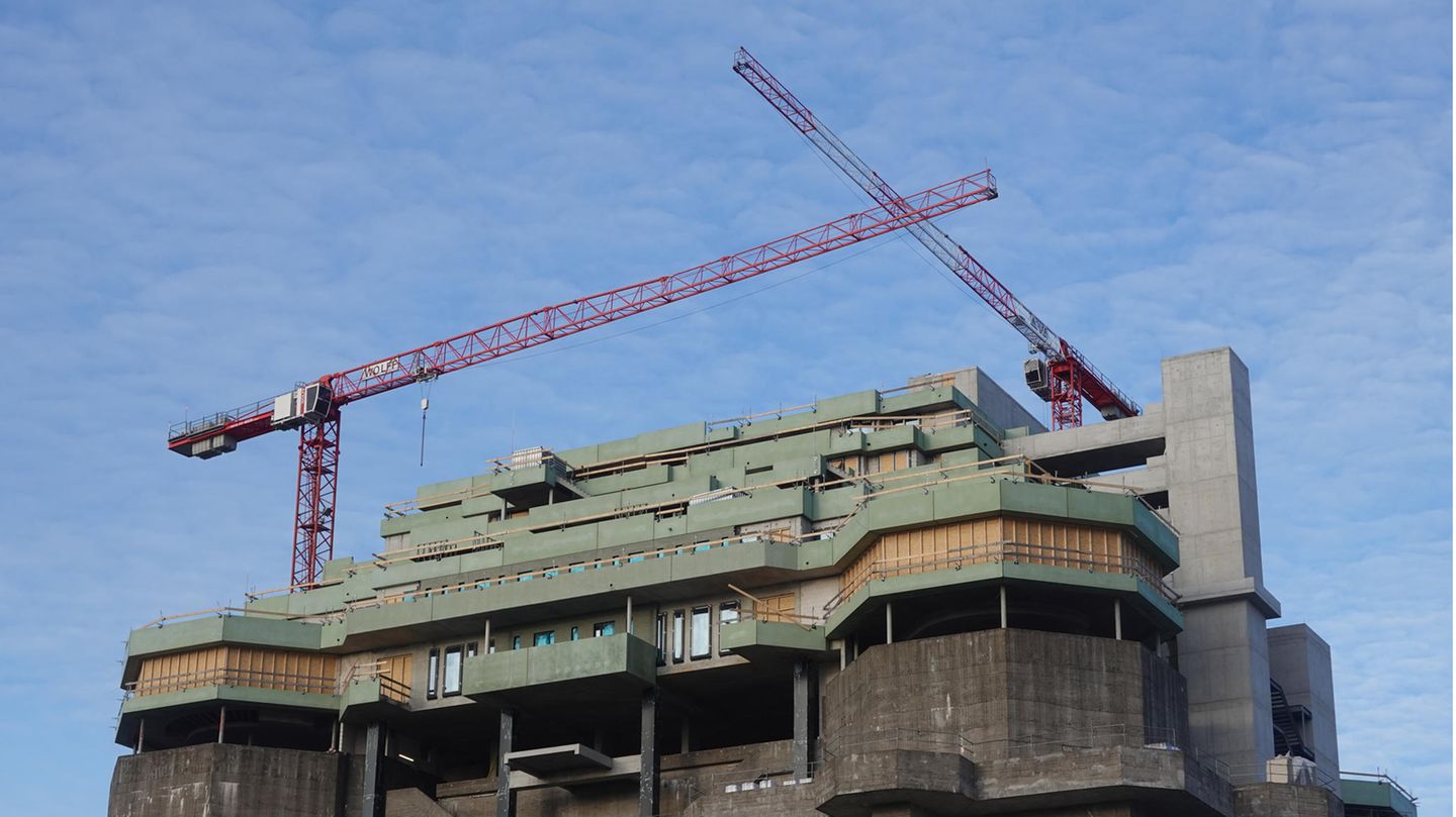 Auf einem dunkelgrauen Hochbunker stehen zwei rote Kräne über dem grün verschalten Rohbau eines Neubaus auf dem Bunkerdach