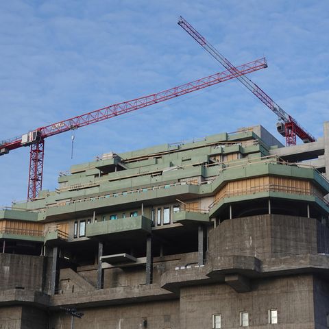 Auf einem dunkelgrauen Hochbunker stehen zwei rote Kräne über dem grün verschalten Rohbau eines Neubaus auf dem Bunkerdach