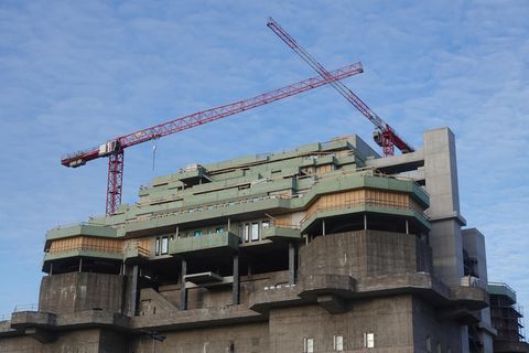 Auf einem dunkelgrauen Hochbunker stehen zwei rote Kräne über dem grün verschalten Rohbau eines Neubaus auf dem Bunkerdach