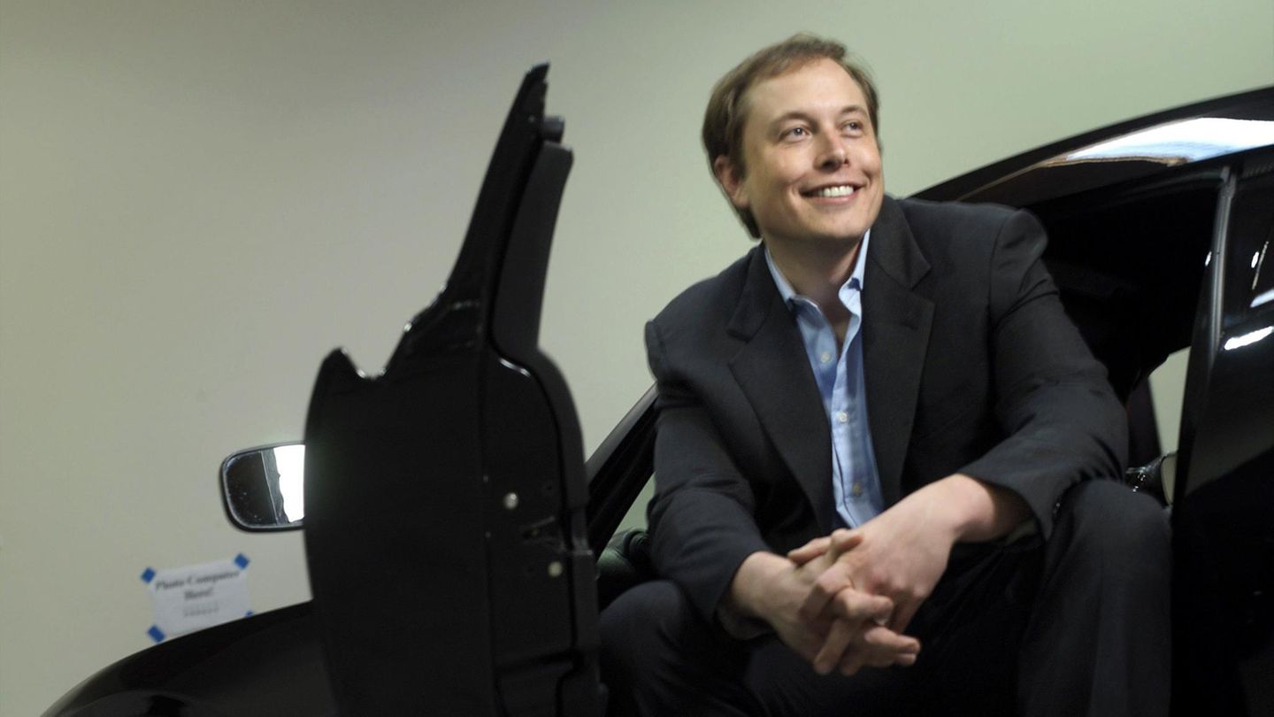 Elon Musk sitzt seitlich auf dem Fahrersitz eines Autos