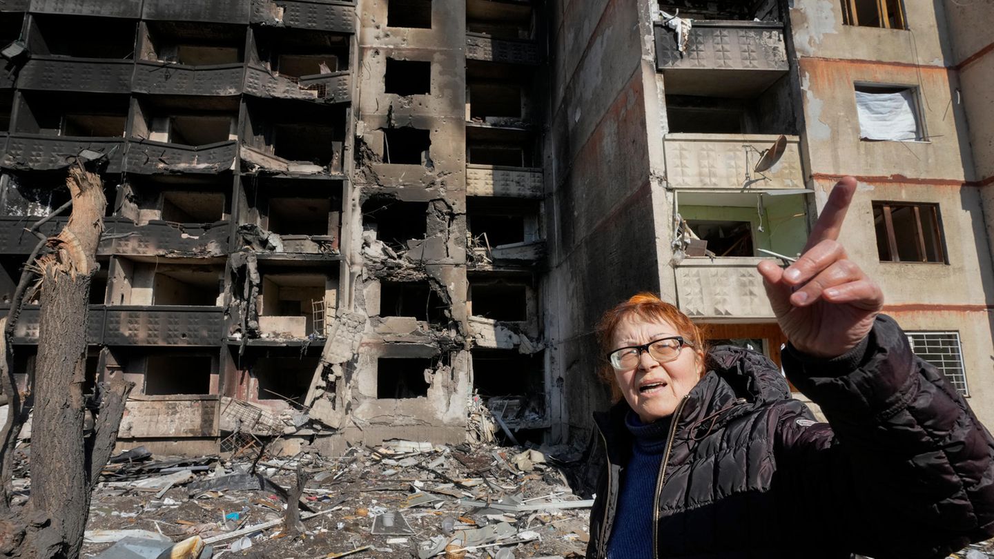 Frau zeigt, woher Granaten kamen, die ihr Haus hinter ihr zerstört haben