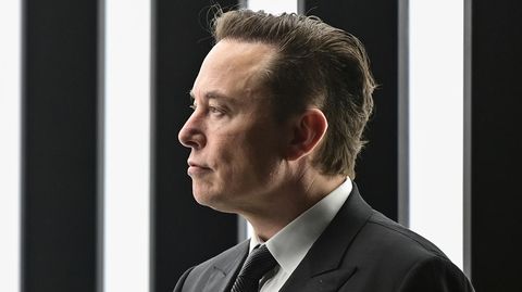 Elon Musk von der Seite vor einer beleuchteten Wand