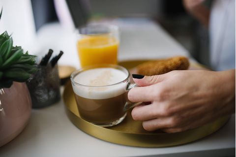 Frauenhand hält Kaffeetasse , im Hintergrund ein Glas Orangensaft