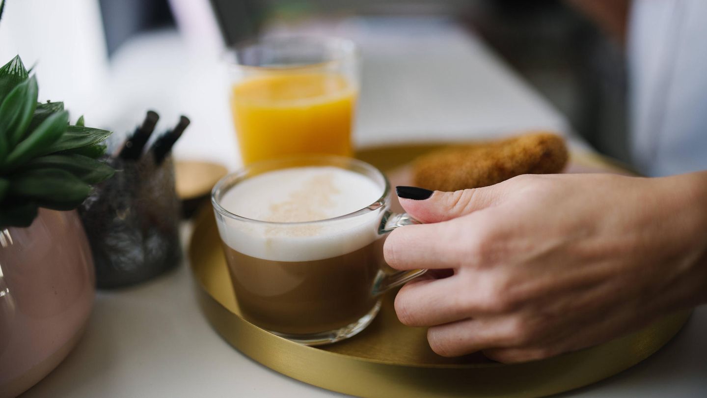 Frauenhand hält Kaffeetasse , im Hintergrund ein Glas Orangensaft