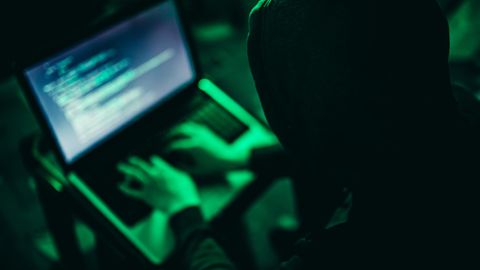 Ein Hacker in dunklem Hoodie an einem Laptop