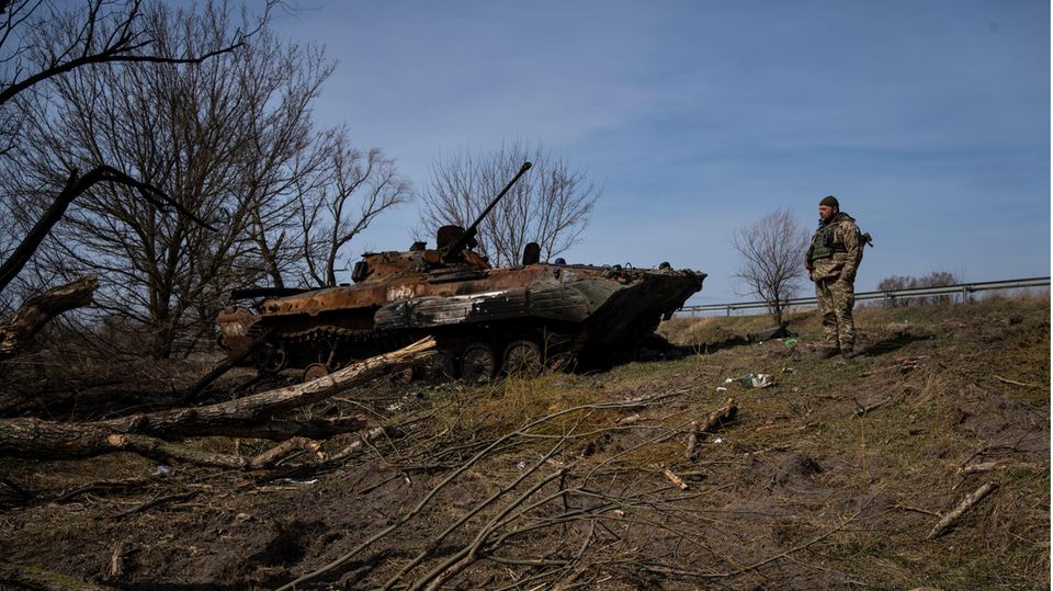 Soldat der Ukraine am Stadtrand von Kiew neben einem zerstörten russischen Kampfpanzer