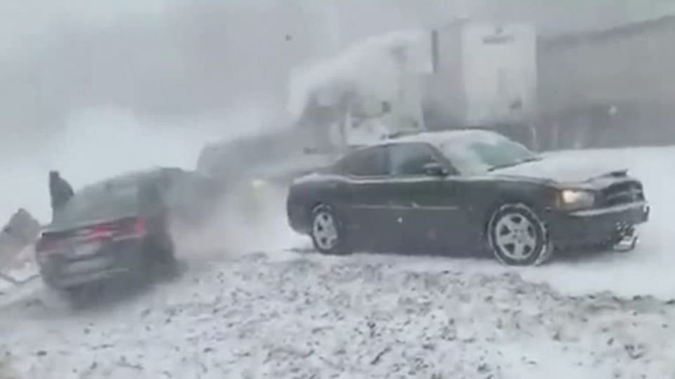 Eine schwarze Limousine steht am Rande einer verschneiten Autobahn, hinter seinem Heck rutscht ein anderes Auto rückwärts vorbei