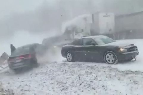 Eine schwarze Limousine steht am Rande einer verschneiten Autobahn, hinter seinem Heck rutscht ein anderes Auto rückwärts vorbei