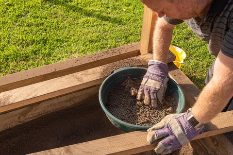 Ein Mann siebt Erde mit einem Gartensieb