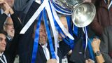 Roman Abramowitsch lacht und streckt im Fußballstadion einen großen Pokal in die Höhe