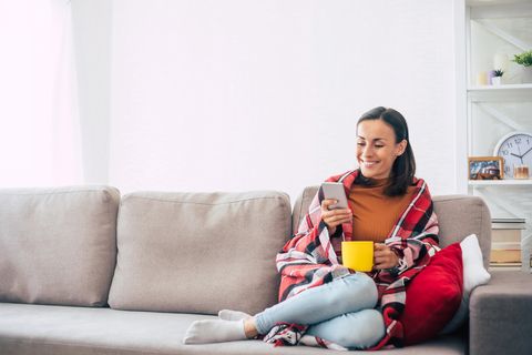 Frau hat ein Smartphone in der Hand und sitzt auf dem Sofa