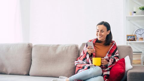 Frau hat ein Smartphone in der Hand und sitzt auf dem Sofa