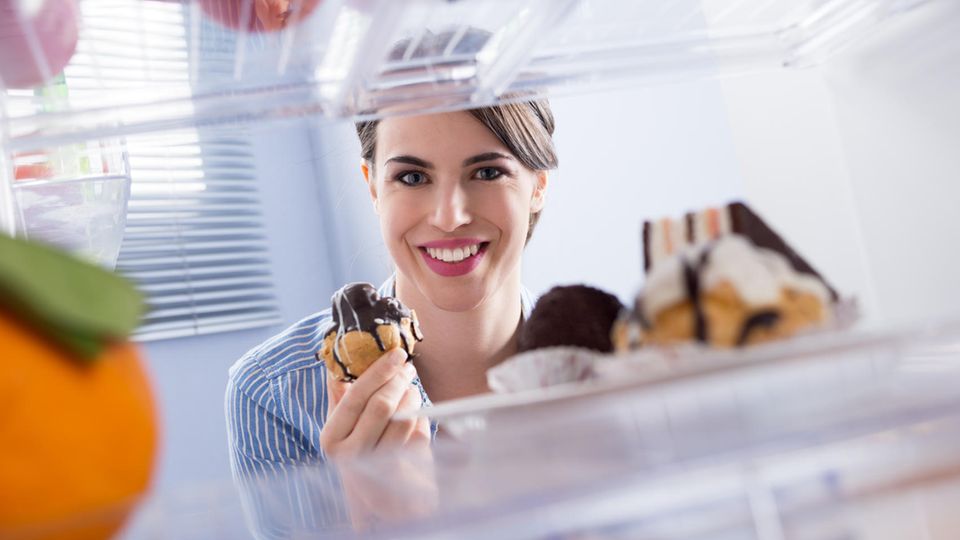 Ein Frau schaut auf Süßigkeiten im Kühlschrank.