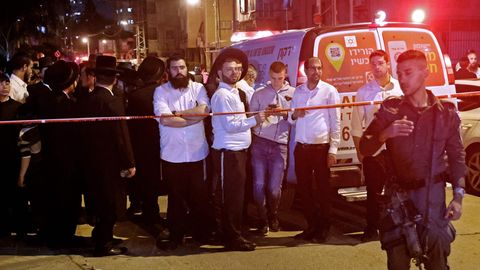 Hinter Absperrband am Heck eines weißen Krankenwagens mit Blaulicht schauen jüdisch-orthodoxe Männer auf einen Soldaten