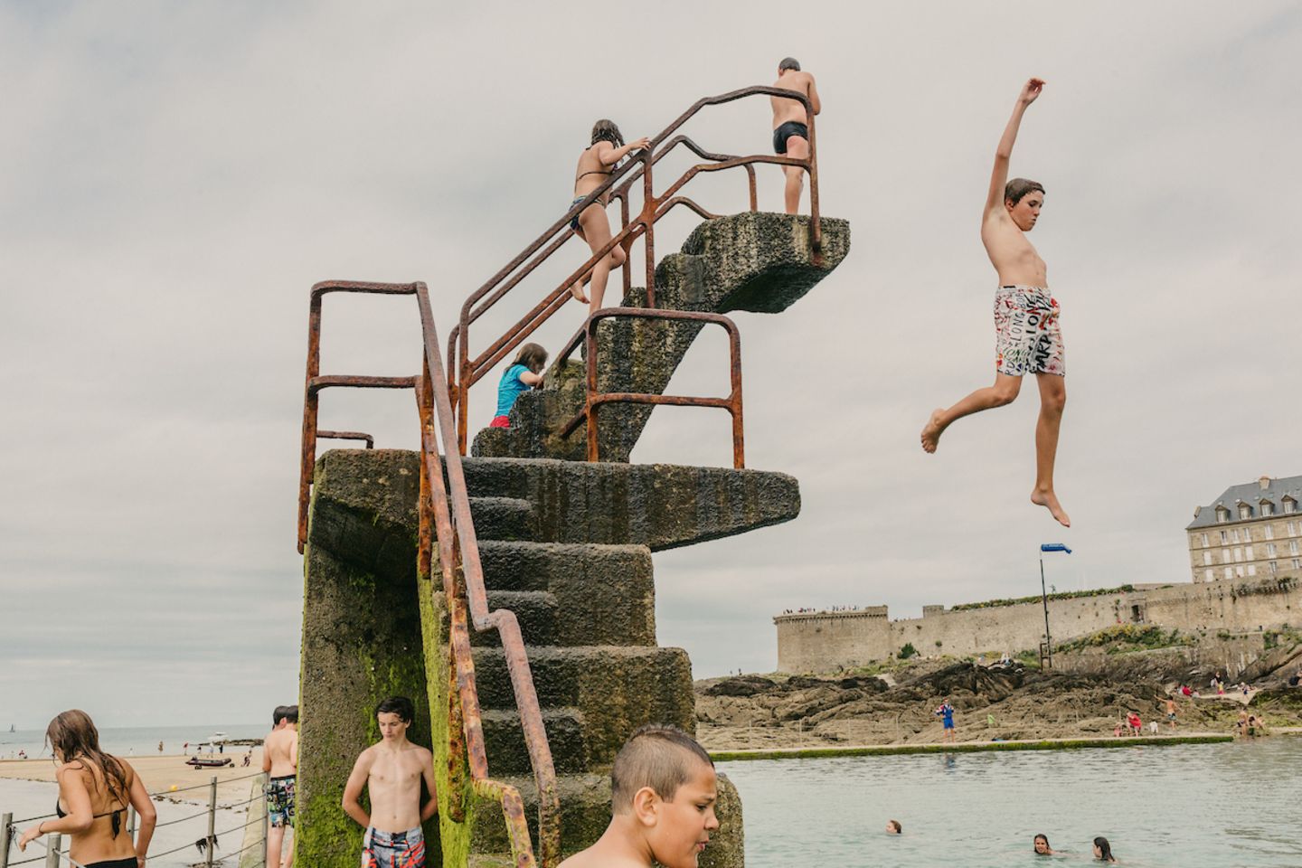 "Swimming and Diving", Ian Teh Kinder schwimmen und tauchen im Lido am Strand von Saint-Malo, einer ummauerten Hafenstadt in der Bretagne im Nordwesten Frankreichs am Ärmelkanal. Ian Teh hat drei Monographien veröffentlicht, "Undercurrents" (2008), "Traces" (2011) und "Confluence" (2014). Seine Arbeiten sind Teil der ständigen Sammlung des Los Angeles County Museum of Art (LACMA), des Museum of Fine Arts, Houston (MFAH) und des Hood Museum in den USA. Ausgewählte Einzelausstellungen umfassen die Jack Shainman Gallery in New York im Jahr 2004, Flowers in London im Jahr 2011 und das Kunsthal Museum in Rotterdam im Jahr 2012.
