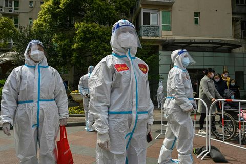 Drei Menschen in weißen Schutzanzügen sowie mit Gesichtsschild und FFP2-Masken schauen im Freien in unterschiedliche Richtungen