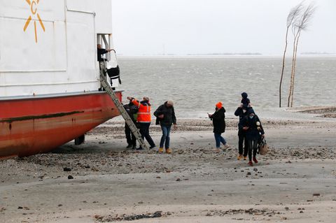 Passagiere klettern über eine Leiter vom Schiff auf den Strand