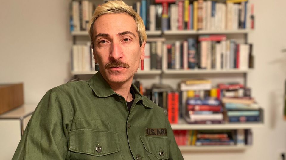 Altan Eskin sitzt an einem Tisch vor einem Bücherregal Altan Eskin sitzt an einem Tisch vor einem Bücherregal