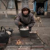 Eine Frau kocht auf einem offenen Feuer vor einem Wohnhaus