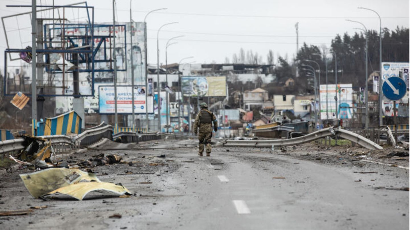 Ein ukrainischer Soldat geht entlang von Leichen auf einer zerstörten Straße.