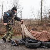 Ein Mitglied der zivilen Schutztruppe schaut auf eine mit einer Decke verhüllte Leiche