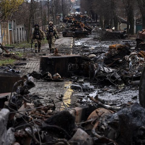 Zwei ukrainische Soldaten gehen auf einer Straße, die übersät ist mit zerstörten russischen Militärfahrzeugen