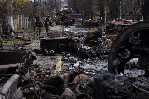 Zwei ukrainische Soldaten gehen auf einer Straße, die übersät ist mit zerstörten russischen Militärfahrzeugen