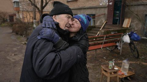 Ukraine, Butscha: Eine Frau küsst einen Mann, während sie auf einem offenen Feuer vor einem Wohnhaus kocht