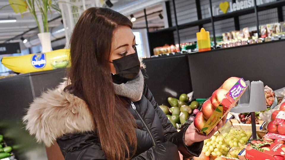 Eine Frau, die Maske trägt, schaut im Supermarkt auf Äpfel