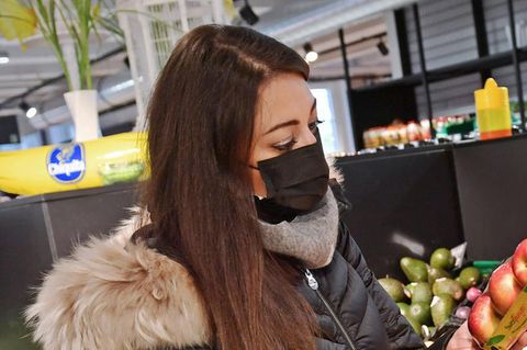 Eine Frau, die Maske trägt, schaut im Supermarkt auf Äpfel