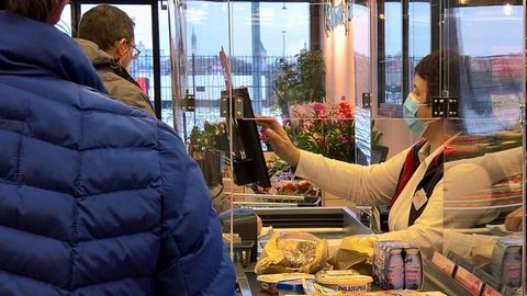 Eine Kassiererin mit Maske im Supermarkt tippt etwas in die Kasse ein