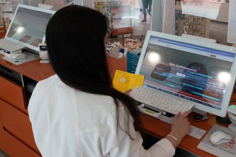 Eine Apothekerin hält einen Impfpass aus Papier in der Hand und gibt die Daten in einen Computer ein