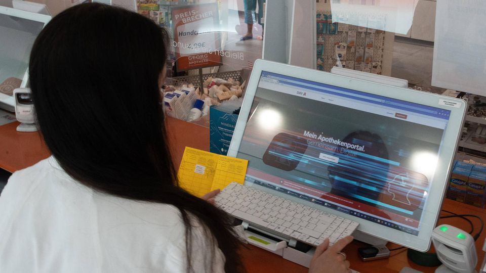 Eine Apothekerin hält einen Impfpass aus Papier in der Hand und gibt die Daten in einen Computer ein