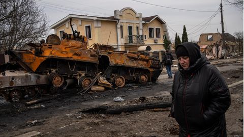 Eine Frau geht an einem zerstörten Militärfahrzeug der russischen Armee vorbei
