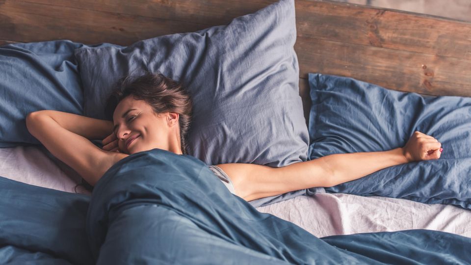 Frau liegt im Bett mit blauer Bettwäsche und streckt sich