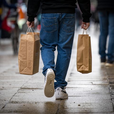 Ein Mann geht über eine Straße und trägt in den Händen zwei Einkaufstaschen
