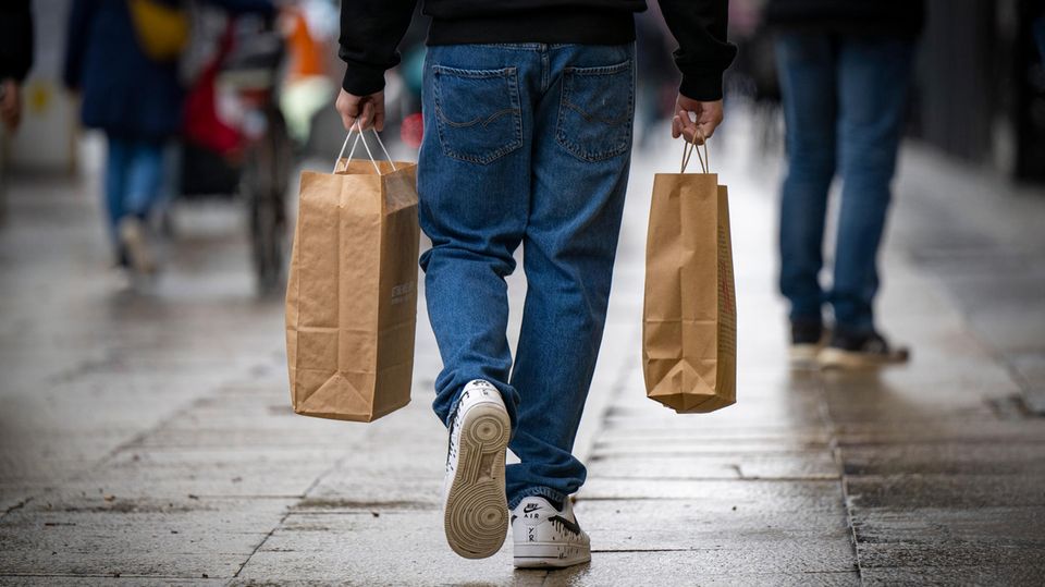 Ein Mann geht über eine Straße und trägt in den Händen zwei Einkaufstaschen