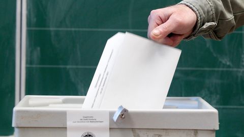Hand wirft einen Wahlzettel in eine Box