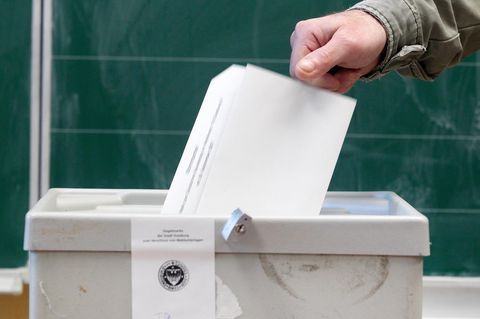 Hand wirft einen Wahlzettel in eine Box