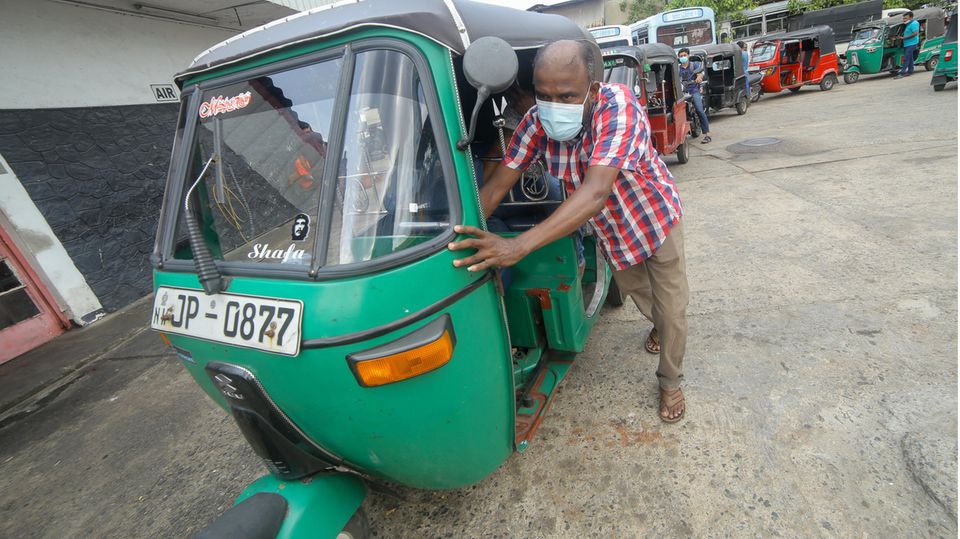 A man pushes his tuk-tuk at a gas station in Sri Lanka.