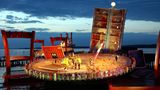 Die Bühne der Bregenzer Festspiele als überdimensionaler Café-Tisch. Riesige Stühle stehen darum. Bild von 2002