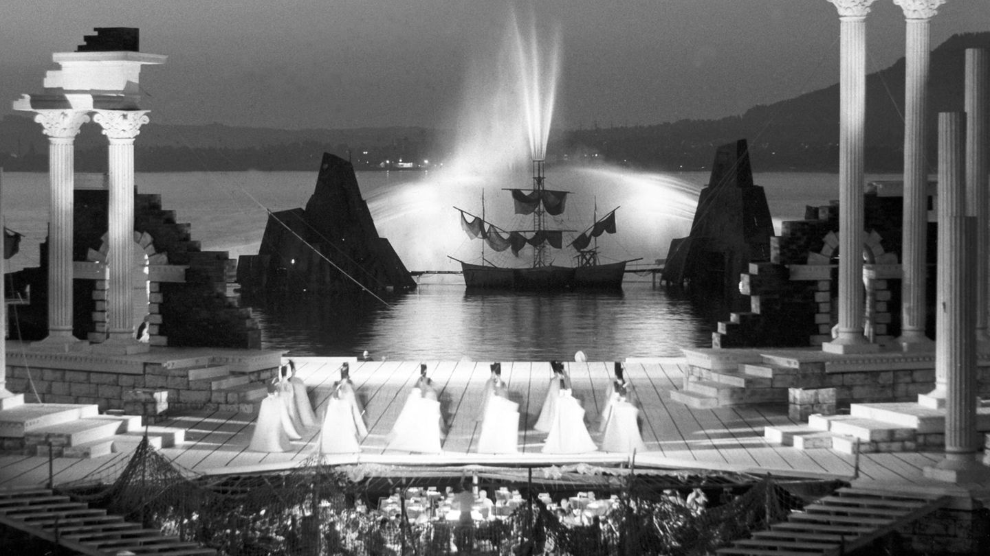 Säulen stehen am Rand der Bühne der Bregenzer Festspiele. Im Hintergrund speit eine Fontäne Wasser. Aufnahme von 1963