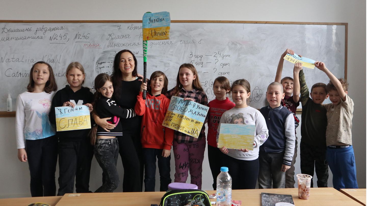 Eine ukrainische Lehrerin steht mit ihren elf Schülerinnen und Schülern wir einer Tafel