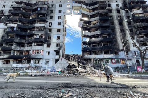 Eine ältere Frau geht mit ihren Hunden an einem durch einen russischen Luftangriff beschädigten Wohnhaus vorbei