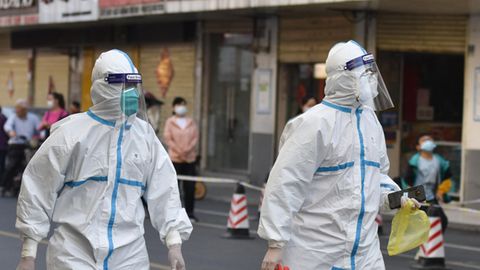 Menschen in weißen Overalls mit FFP2-Masken und Gesichtsschilden gehen auf einer Straße durch eine Großstadt