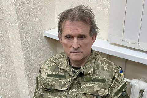 Ein älterer weißer Mann mit zerzaustem grauen Haar sitzt in Tarnfleck-Uniform und Handschellen auf einem Stuhl
