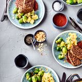 Veganer Nussbraten mit Bratensauce und Gemüse      Zutaten für 4 Portionen:   Für den Nussbraten: 100 g Belugalinsen, 250 g ganze Nüsse (z.B. eine Mischung aus Haselnüssen, Pekannüssen, Walnüssen), 200 g rote oder orange Möhren, 1 rote Zwiebel, 20 g glatte Petersilie, 2 EL Sojasauce, 2 EL Senf, 2 EL Stärke, 150 g Glutenfreie Haferflocken blütenzart, 2 EL Buchweizenmehl, 1 gehäufter EL Hackfleischgewürz, Salz, Pfeffer  Für die Sauce: 150 g Champignons, 150 g rote oder orange Karotten, 200 g Knollensellerie, 1 rote Zwiebel, 1 Knoblauchzehe,  2 EL Speiseöl, 3 EL Sojasauce, 1 TL Tomatenmark, 1 TL Zucker, 2 EL Balsamicoessig, 1 TL Senf, 200 ml Rotwein, 400 ml Gemüsefond oder Gemüsebrühe, 2 Lorbeerblätter Salz, Pfeffer, Muskat, Paprika edelsüß      Zubereitung:   Linsen 20 Minuten in Salzwasser garen, abgießen und abtropfen lassen. Nuss-Mischung sehr fein im Mixer zerkleinern und in eine Schüssel geben. Möhren und Zwiebel schälen und in grobe Scheiben schneiden. Petersilie waschen und verlesen. Gemüse, Petersilie, 50 ml Wasser, Sojasauce, Senf und Stärke im Mixer zu einer Masse verarbeiten. Zusammen mit Haferflocken, Linsen und Mehl zur Nuss-Mischung geben. Vorsichtig miteinander vermengen und mit den Gewürzen abschmecken. Kastenform mit Backpapier auskleiden (Tipp: Backpapier vorher einmal komplett zerknüllen und wieder auseinanderstreichen – dann ist es formbarer). Masse in eine Kastenform (25 cm) einfüllen und backen.  Derweil das Gemüse putzen, ggf. schälen und in grobe Würfel oder Scheiben schneiden. Speiseöl in einem Topf erhitzen und Champignons, Möhren und Knollensellerie 5 Minuten rundherum anbraten – es dürfen braune Stellen für das Röstaroma zu sehen sein. Zwiebel und Knoblauch hinzufügen und weitere 3 Minuten weiterbraten. Sojasauce, Tomatenmark, Zucker, Balsamico und Senf hinzufügen, kräftig umrühren und kurz weiterbraten. Anschließend mit Rotwein und Gemüsefond ablöschen, Lorbeerblätter dazugeben und 20 Minuten köcheln lassen.   Lorbeerblätter wieder entfernen. Mit dem Pürierstab das Gemüse sehr fein zerkleinern. Mit dem Zufügen von Wasser erhält man die gewünschte Konsistenz der Sauce. Mit den Gewürzen abschmecken und mit dem Nussbraten servieren.  Dazu passen Kartoffelpüree und Rosenkohl.