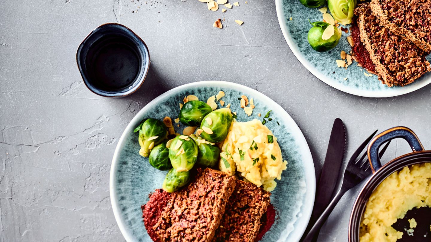 Veganer Nussbraten mit Bratensauce und Gemüse      Zutaten für 4 Portionen:   Für den Nussbraten: 100 g Belugalinsen, 250 g ganze Nüsse (z.B. eine Mischung aus Haselnüssen, Pekannüssen, Walnüssen), 200 g rote oder orange Möhren, 1 rote Zwiebel, 20 g glatte Petersilie, 2 EL Sojasauce, 2 EL Senf, 2 EL Stärke, 150 g Glutenfreie Haferflocken blütenzart, 2 EL Buchweizenmehl, 1 gehäufter EL Hackfleischgewürz, Salz, Pfeffer  Für die Sauce: 150 g Champignons, 150 g rote oder orange Karotten, 200 g Knollensellerie, 1 rote Zwiebel, 1 Knoblauchzehe,  2 EL Speiseöl, 3 EL Sojasauce, 1 TL Tomatenmark, 1 TL Zucker, 2 EL Balsamicoessig, 1 TL Senf, 200 ml Rotwein, 400 ml Gemüsefond oder Gemüsebrühe, 2 Lorbeerblätter Salz, Pfeffer, Muskat, Paprika edelsüß      Zubereitung:   Linsen 20 Minuten in Salzwasser garen, abgießen und abtropfen lassen. Nuss-Mischung sehr fein im Mixer zerkleinern und in eine Schüssel geben. Möhren und Zwiebel schälen und in grobe Scheiben schneiden. Petersilie waschen und verlesen. Gemüse, Petersilie, 50 ml Wasser, Sojasauce, Senf und Stärke im Mixer zu einer Masse verarbeiten. Zusammen mit Haferflocken, Linsen und Mehl zur Nuss-Mischung geben. Vorsichtig miteinander vermengen und mit den Gewürzen abschmecken. Kastenform mit Backpapier auskleiden (Tipp: Backpapier vorher einmal komplett zerknüllen und wieder auseinanderstreichen – dann ist es formbarer). Masse in eine Kastenform (25 cm) einfüllen und backen.  Derweil das Gemüse putzen, ggf. schälen und in grobe Würfel oder Scheiben schneiden. Speiseöl in einem Topf erhitzen und Champignons, Möhren und Knollensellerie 5 Minuten rundherum anbraten – es dürfen braune Stellen für das Röstaroma zu sehen sein. Zwiebel und Knoblauch hinzufügen und weitere 3 Minuten weiterbraten. Sojasauce, Tomatenmark, Zucker, Balsamico und Senf hinzufügen, kräftig umrühren und kurz weiterbraten. Anschließend mit Rotwein und Gemüsefond ablöschen, Lorbeerblätter dazugeben und 20 Minuten köcheln lassen.   Lorbeerblätter wieder entfernen. Mit dem Pürierstab das Gemüse sehr fein zerkleinern. Mit dem Zufügen von Wasser erhält man die gewünschte Konsistenz der Sauce. Mit den Gewürzen abschmecken und mit dem Nussbraten servieren.  Dazu passen Kartoffelpüree und Rosenkohl.