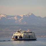 Eine Fähre überquert vor Bergkulisse den Bodensee
